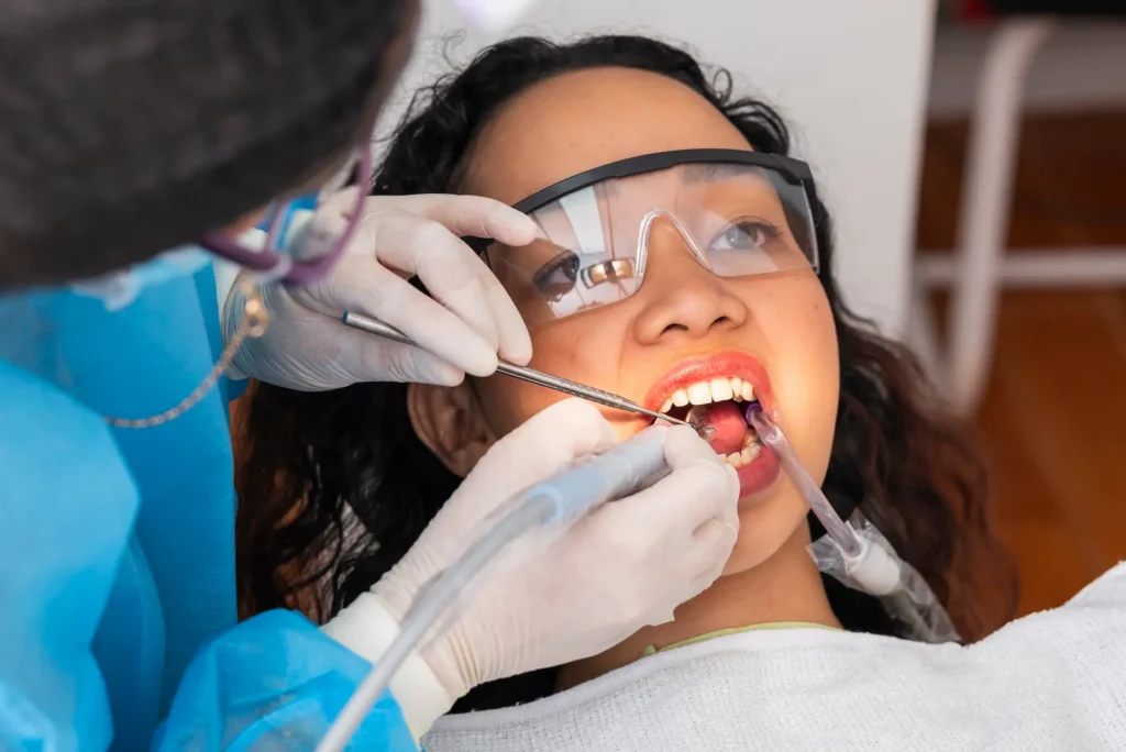 young woman undergoes professional dental cleaning using an ultrasonic scaler, dental mirror, and suction during oral prophylaxis.