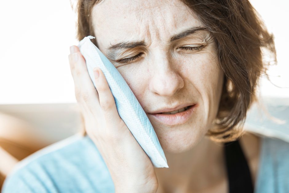 person applying a cold compress to the jaw for TMJ pain relief